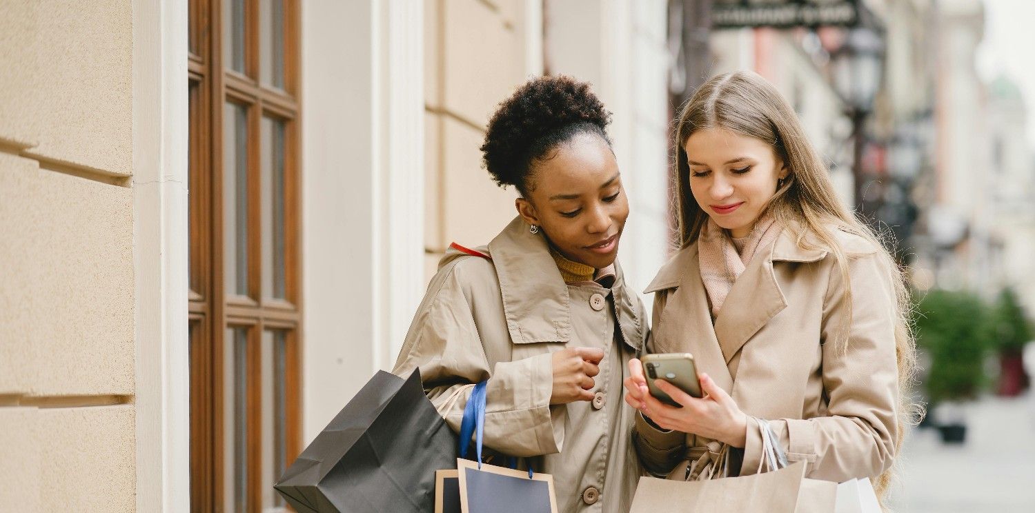 Two shoppers on a city street checking a phone for the best local café